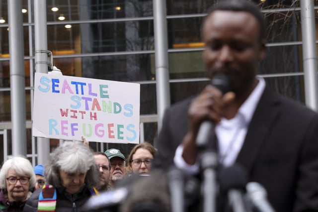 Signs are seen as Tshishiku Henry, a former refugee and Washington State Delegate for the Refugee Congress, speaks during a rally outside the U.S District Court after a federal judge blocked President Donald Trump's effort to halt the nation's refugee admissions system, Tuesday, Feb. 25, 2025 in Seattle. (AP Photo/Ryan Sun)