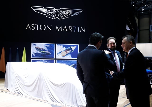 People talk in front of covered cars on the Aston Martin stand during the 87th International Motor Show at Palexpo in Geneva, Switzerland, March 7, 2017.
