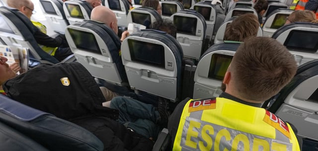 Ein Beamter der Bundespolizei sitzt an Bord des Abschiebefluges neben einem Migranten (l.)
