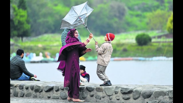 A woman and boy share a moment of laughter while trying to control a flipped umbrella amid windy and rainy weather at Sukhna Lake in Chandigarh on Thursday. (Ravi Kumar/HT)