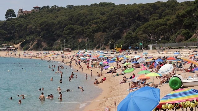 Touristen sonnen sich und spielen im Wasser am Strand von Fenals in Lloret de Mar.