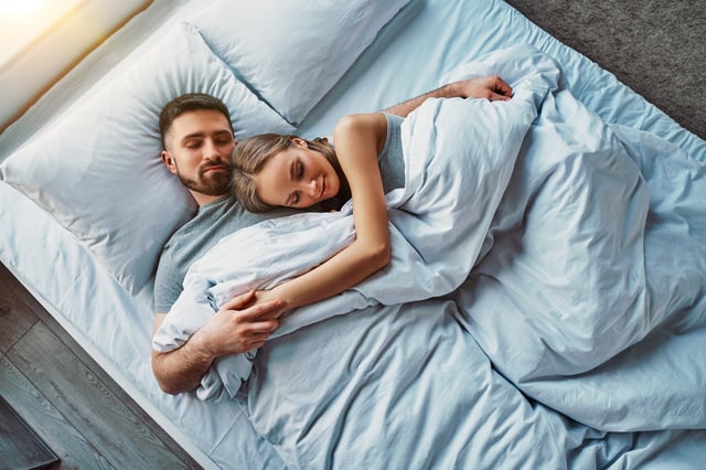 A stock image of a couple sleeping in bed together.