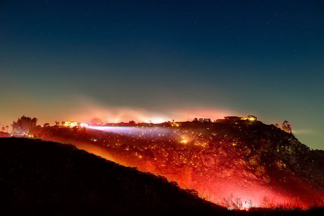 In this long exposure photo, fire smolders on a hillside during the Lilac fire in unincorporated San Diego County, California on January 21, 2025.