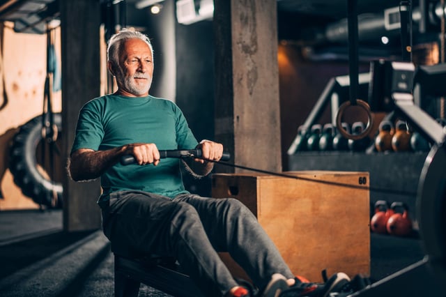 Active senior man doing an exercise on a rowing machine in a gym gym.