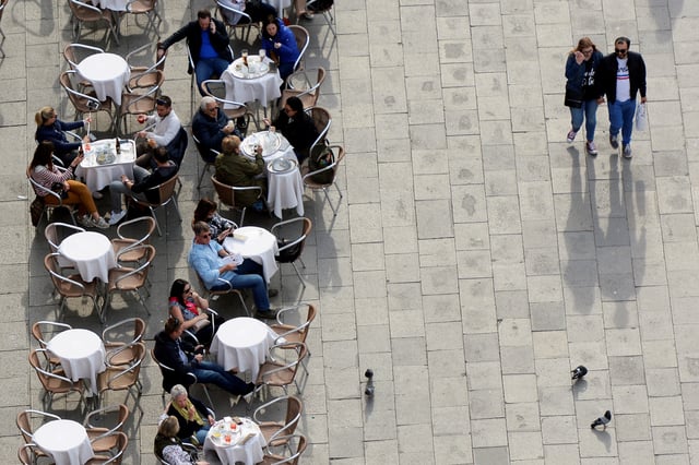 People sit at a cafe in St.Mark's Square in Venice, Italy, April 2, 2019. REUTERS/Guglielmo Mangiapane/File Photo