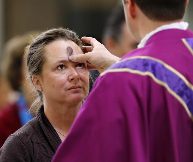 Rev. Stephen Hamilton, pastor, traces a cross on the forehead of a woman during an Ash Wednesday service at St. Monica Catholic Church in Edmond, Oklahoma on Wednesday, March 5, 2014.