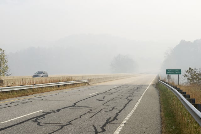 A stock photo of a car driving on a bridge over the Nantahala River/Fontana Lake in Swain County, North Carolina. The air is filled with smoke from nearby forest fires in Almond, North Carolina, USA - November 11, 2016.