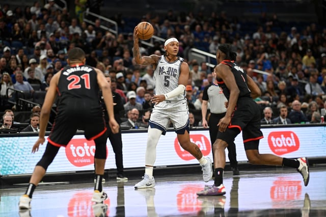 Orlando Magic forward Paolo Banchero (5) is defended by Toronto Raptors center Orlando Robinson (21) and forward Jonathan Mogbo, right, during the first half of an NBA basketball game, Tuesday, March 4, 2025, in Orlando, Fla. (AP Photo/Phelan M. Ebenhack)