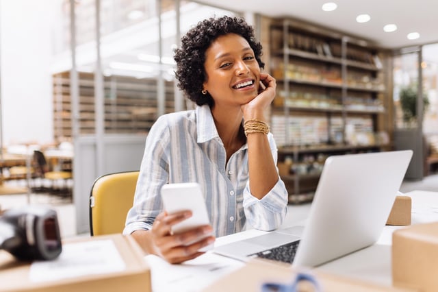 In this stock image, a store owner smiles at the camera while working in a warehouse.