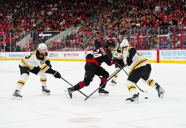 Mar 6, 2025; Raleigh, North Carolina, USA;  Carolina Hurricanes center Seth Jarvis (24) takes the puck inside of Boston Bruins defenseman Ian Mitchell (14) and center Charlie Coyle (13) during the first period at Lenovo Center. Mandatory Credit: James Guillory-Imagn Images
