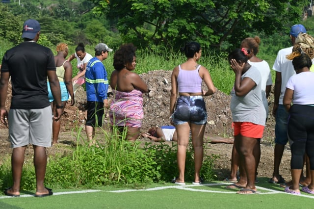People look at the body of a woman found in the neighborhood where at least 22 people were killed on the eve in Guayaquil, Ecuador, on March 7, 2025. Rival factions of an Ecuadoran drug trafficking gang fought Thursday in the violent port city of Guayaquil, leaving at least 22 people dead, officials said.