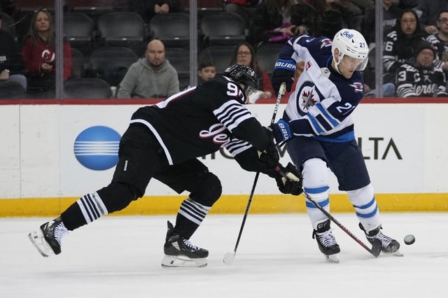 New Jersey Devils' Tomas Tatar, left, fights for control of the puck with Winnipeg Jets' Nikolaj Ehlers (27) during the first period of an NHL hockey game Friday, March 7, 2025, in Newark, N.J. (AP Photo/Frank Franklin II)