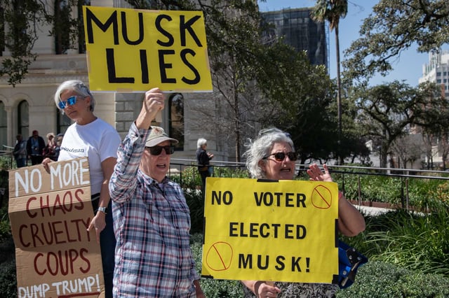 Peter Baughman, left, and Sharon Baughman, right protest against Elon Musk and President Donald Trump&#39;s firing of federal workers, at a rally with about 200 other protestors, in front of City Hall on Tuesday, March 4, 2025 in San Antonio. The protest was organized by Bexar Democrats and 50501 to protest against the firing of federal workers and executive order overreach.