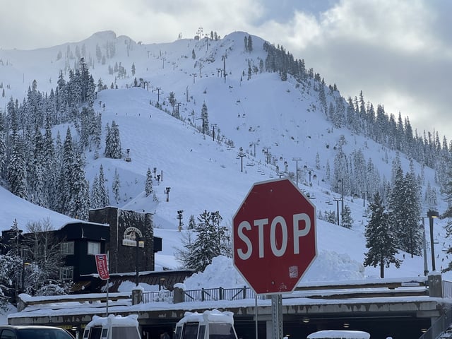 Stop sign in front of snow-covered ski slopes and chairlifts at a mountain resort on a cloudy morning, Olympic Valley, California, February 14, 2025.