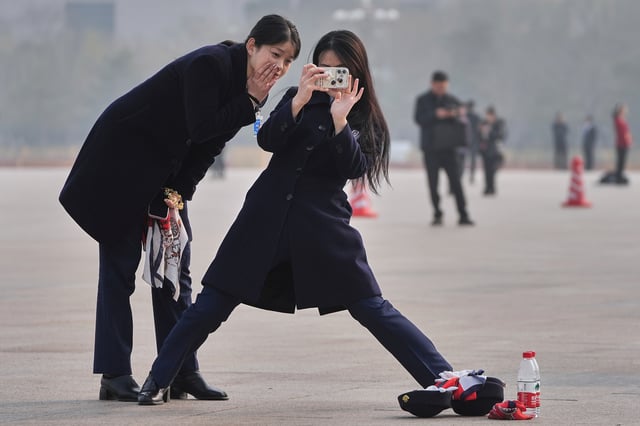 A hostess uses a smartphone to take photo of her colleague at Tiananmen Square during the closing of the Chinese People's Political Consultative Conference in Beijing, Monday, March 10, 2025. (AP Photo/Andy Wong)