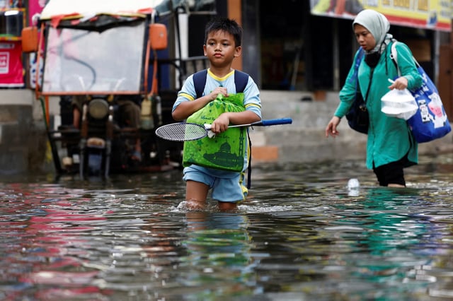 People walk through water at a flooded area affected by rising sea levels and land subsidence in North Jakarta, Indonesia, November 20, 2024. REUTERS/Willy Kurniawan/File Photo