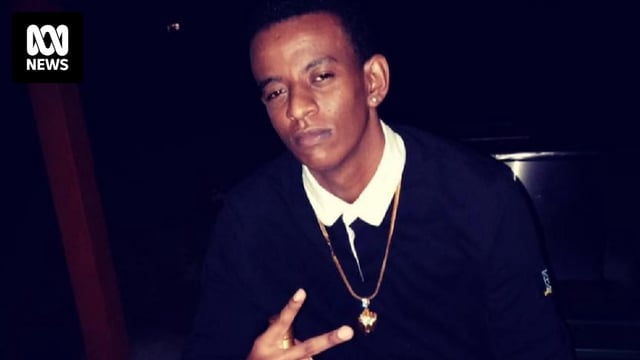 A young man crouched and holding two fingers up