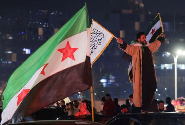 A person holds flags as people celebrate after the Kurdish-led and U.S.-backed Syrian Democratic Forces (SDF), which controls much of Syria's oil-rich northeast, has signed a deal agreeing to integrate into Syria's new state institutions, the Syrian presidency said on Monday, in Damascus, Syria March 11, 2025. REUTERS/Khalil Ashawi/File Photo