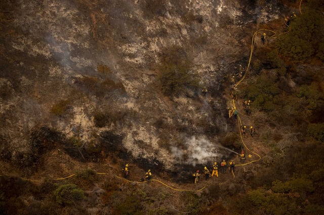 A group of firefighters traverse a steep hill while battling the Palisades Fire in the Mandeville Canyon neighborhood of Los Angeles in January. 
