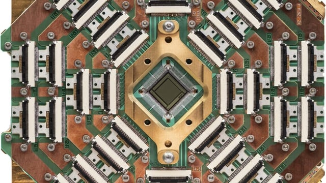 Image of a complex pattern of circuitry and connections, primarily golden in color, surrounding a black square chip in the center.