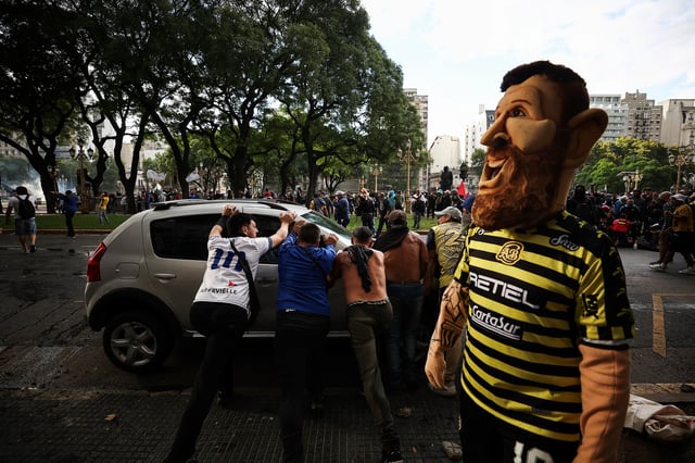 Demonstrators push against a car, next to a demonstrator wearing a costume in the likeness of Argentinian footballer Lionel Messi, as football fans join the weekly protest of retirees against Argentinian President Javier Milei's adjustment policies, near the National Congress in Buenos Aires, Argentina March 12, 2025. REUTERS/Agustin Marcarian