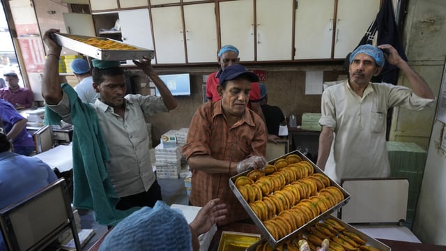 Workers carry Gujiyas, a sweet dish, specially made for the Holi festival, before packing for customers at a sweet shop in New Delhi.