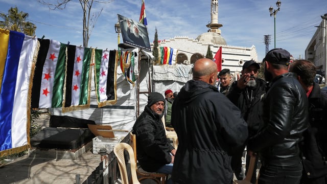 Druze men gather by a newsstand selling flags of Syria and the Druze community at Al Karama Square in city of Sweida, Syria