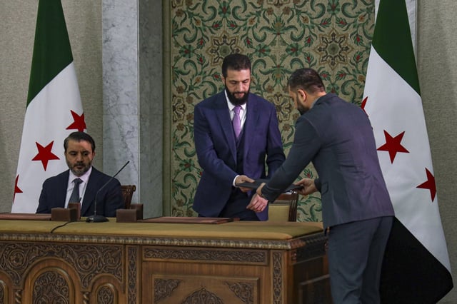 Syria's interim president Ahmad Al-Sharaa, center, prepares to sign a temporary constitution for the country in Damascus, Syria, Thursday March 13, 2025. At left foreign minister Asaad Hassan al-Shiban.(AP Photo/Omar Albam)