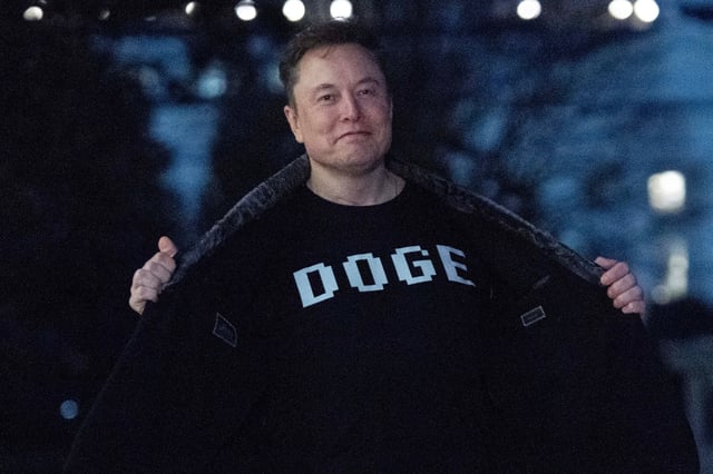 Elon Musk flashes his t-shirt that reads &#34;DOGE&#34; to the media as he walks on South Lawn of the White House, in Washington, Sunday, March 9, 2025.