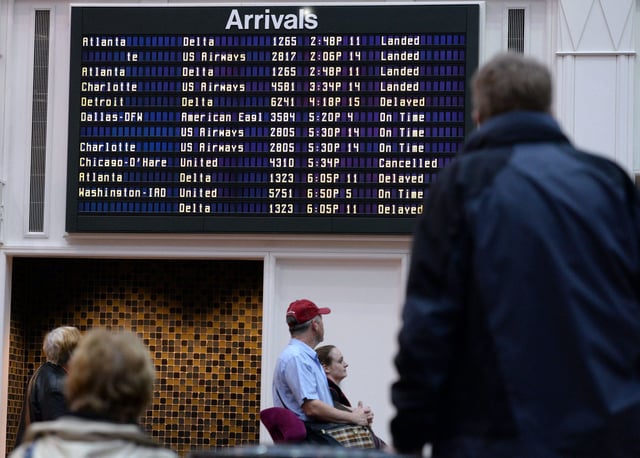 People awaiting arrivals at Savannah/Hilton Head International Airport look at the board as a few flights are marked as delayed, landed or canceled.