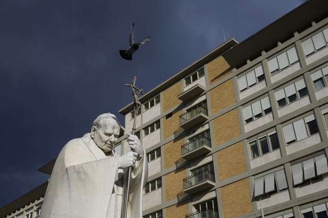 A marble statue of late Pope John Paul II is backdropped by the Agostino Gemelli Polyclinic in Rome, Saturday, Feb. 15, 2025, where Pope Francis was hospitalized Friday, Feb. 14, after a weeklong bout of bronchitis worsened and is receiving drug therapy for a respiratory tract infection. (AP Photo/Alessandra Tarantino)