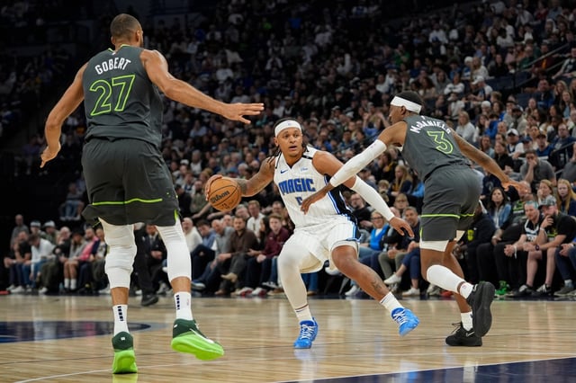 Orlando Magic forward Paolo Banchero (5) works toward the basket as Minnesota Timberwolves center Rudy Gobert (27) and forward Jaden McDaniels (3) defend during the first half of an NBA basketball game, Friday, March 14, 2025, in Minneapolis. (AP Photo/Abbie Parr)