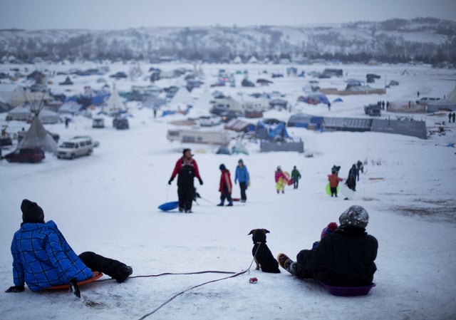 FILE - In this Thursday Dec. 1, 2016 file photo, the Oceti Sakowin camp where people have gathered to protest the Dakota Access oil pipeline stands in the background as a children sled down a hill in Cannon Ball, N.D. (AP Photo/David Goldman, File)
