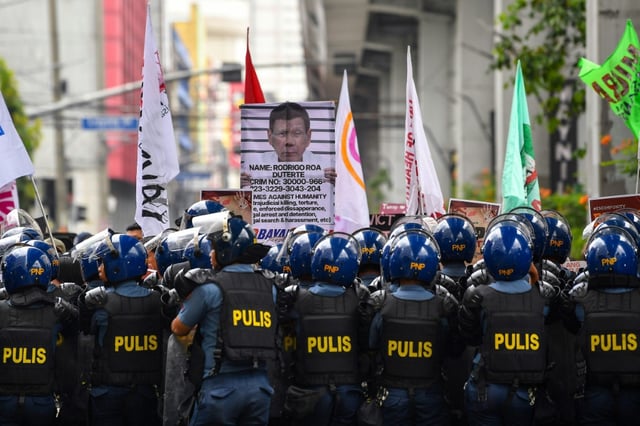 Protesters carrying a placard showing former president Rodrigo Duterte are blocked by anti-riot police near the presdiential palace in Manila