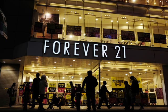 FILE - Shoppers walk by a Forever 21 clothing store, Thursday, Oct. 24, 2019, in Tokyo, as the liquidation sale signs are posted on the storefront. (AP Photo/Kiichiro Sato, file)