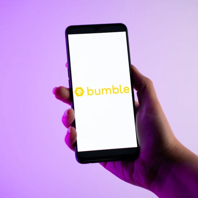 A person holds a smartphone with Bumble's logo on the screen. 