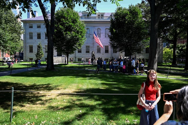 A passerby poses for a photo with a Harvard tour group and the statue of John Harvard in the background on Harvard Yard, on the first day of the fall semester at Harvard University in Cambridge, Massachusetts, U.S., September 3, 2024.  REUTERS/Nicholas Pfosi/File Photo