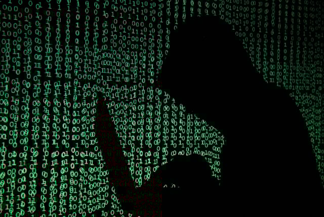 A hooded man holds a laptop computer as cyber code is projected on him in this illustration picture taken on May 13, 2017. REUTERS/Kacper Pempel/Illustration/File Photo