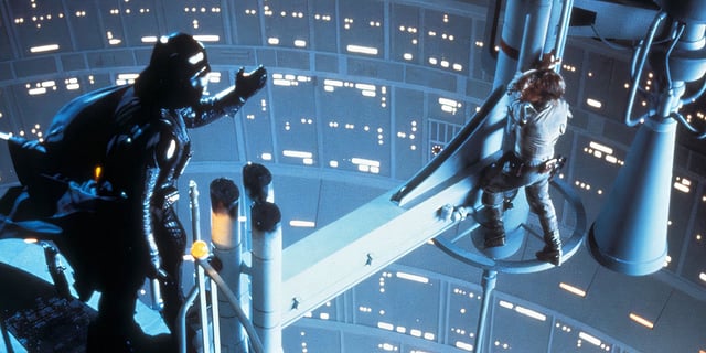 David Prowse as Darth Vader reaches out to Mark Hamil as Luke Skywalker, who is standing on a platform in Star Wars: Episode V - The Empire Strikes Back (1980). 