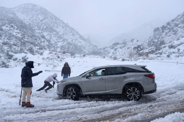 A person helps push out a vehicle that became stuck in the snow on a roadway in the San Gabriel Mountains in the Angeles National Forest, California, on February 24, 2023.