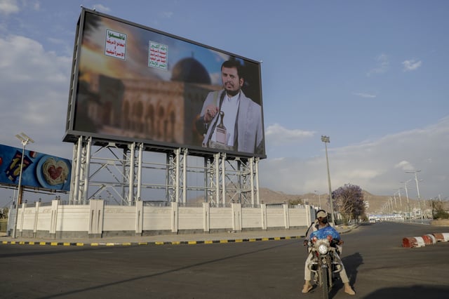 Yemenis pass under a street billboard displaying a picture of Abdul Malik al-Houthi, the leader of the Houthi movement, in Sanaa, Yemen, Tuesday, March 18, 2025. Arabic reads, "death to America, death to Israel". (AP Photo/Osamah Abdulrahman)