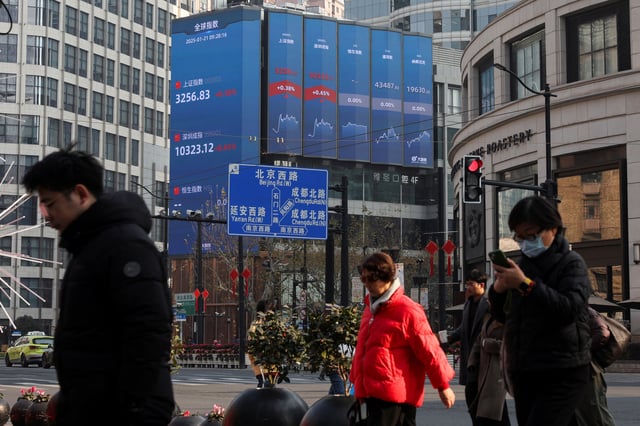 Pedestrians wait for a street signal on a sidewalk as an electronic billboard shows the Shanghai and Shenzhen stock indexes in Shanghai, China January 21, 2025.  REUTERS/Go Nakamura/File Photo
