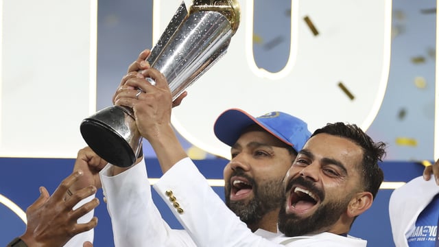 India's Virat Kohli, right, and captain Rohit Sharma celebrate with the winners trophy on the podium.