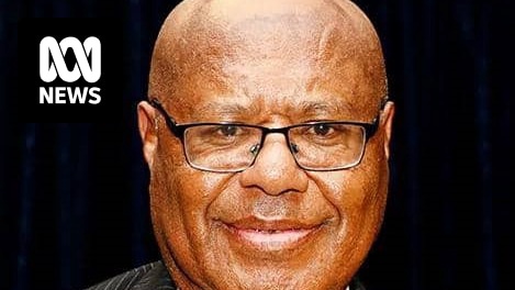 Headshot of a bald black man wearing glasses, suit and tie