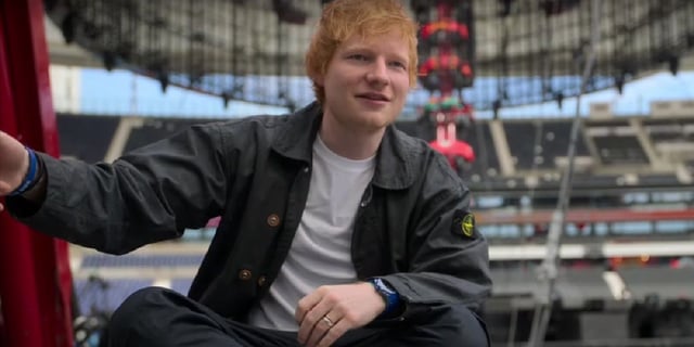 Ed Sheeeran in the sum of it all sitting outside in a black jacket.