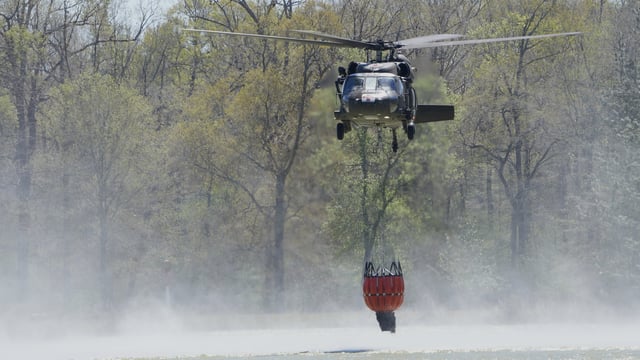 A helicopter drops a bucket to gather water to battle the Pauline Road wildfire Thursday, March 20, 2025, in Cleveland, Texas.