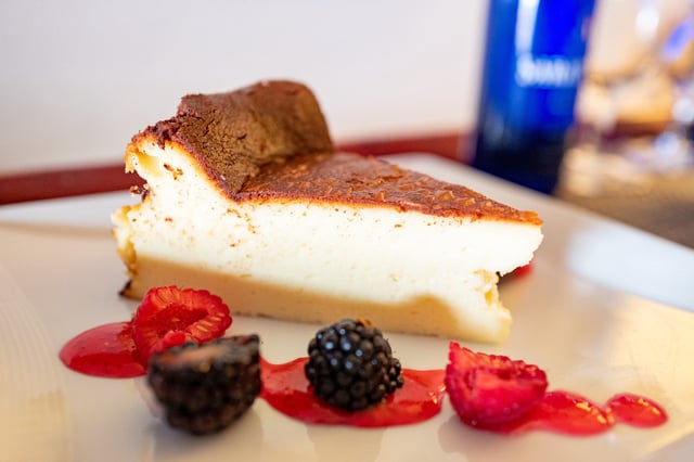 A close-up of a slice of cheesecake with a golden-brown top can be seen alongside fresh raspberries and blackberries on a white plate, San Jose, California, August 3, 2024. (Photo by Smith Collection/Gado/Getty Images)
