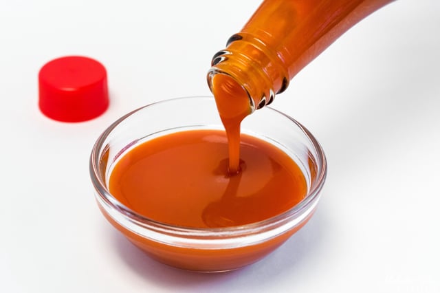In this stock image, a bottle of red hot sauce is poured into a glass bowl.