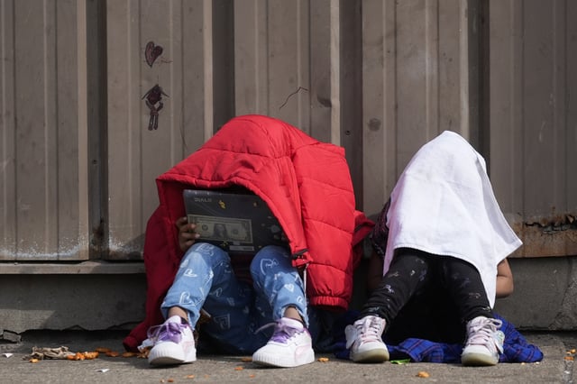 FILE - Children cover their heads as they sit outside of a migrant shelter Wednesday, March 13, 2024, in the Pilsen neighborhood of Chicago. (AP Photo/Erin Hooley, File)