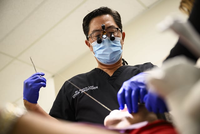 Dr. Melvin Lee, left, performs sutures after a tooth extraction for a patient at his dental clinic in Ottawa, on Wednesday, Aug. 7, 2024. 